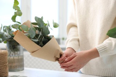 Çiçekçi, çiçekçide beyaz masada okaliptüs dallarından güzel bir buket yapıyor.