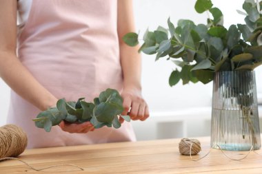 Çiçekçinin ahşap masasında okaliptüs dallarından güzel bir buket yapıyor.