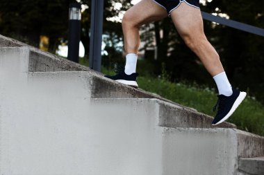 Spor giyimli atletik genç adam merdivenlerden yukarı koşuyor, yakın plan.