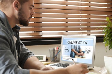 Çevrimiçi çalışma. Masada e-öğrenim için dizüstü bilgisayar kullanan bir adam