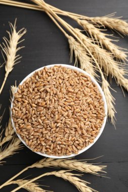 Kasede buğday taneleri ve siyah tahta masada çiviler, düz uzanmış.