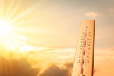 Güneşli bir günde, turuncu gökyüzüne karşı termometrede son derece yüksek sıcaklık. Şiddetli sıcak yaz havası