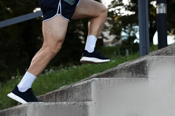 Spor giyimli atletik genç adam merdivenlerden yukarı koşuyor, yakın plan.