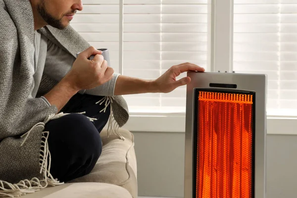 Evinde elektrikli ısıtıcının yanında bir bardak sıcak içeceği olan adam, yakın çekim.