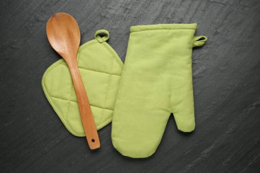 Yeşil fırın eldiveni, ahşap kaşık ve tutacağı koyu dokulu masa, düz yatıyordu.