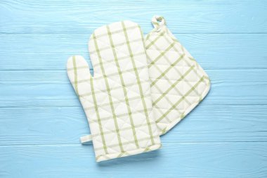 Fırın eldiveni ve tutacağı açık mavi ahşap arka planda, düz yerde.