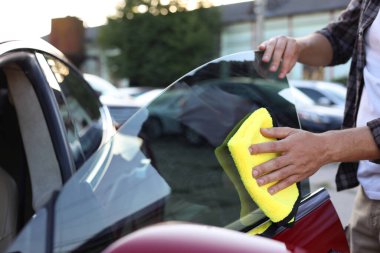 Arabanın yan camını sarı mikrofiber bez ile silen adam, yakın plan.