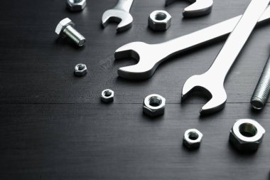 Bir sürü metal anahtar, cıvata ve somun siyah ahşap masada, yakın plan. Metin için boşluk