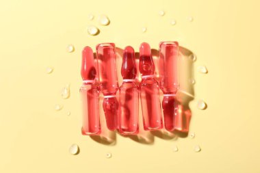 Sarı zemin üzerinde sıvı ve su damlaları olan cam ampuller düz yatıyordu.