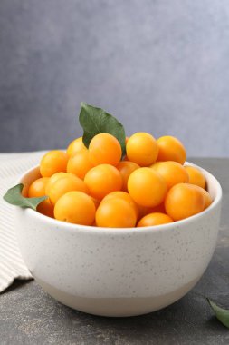 Olgun sarı kiraz erikleri ve yapraklar gri masada, yakın plan. Metin için boşluk