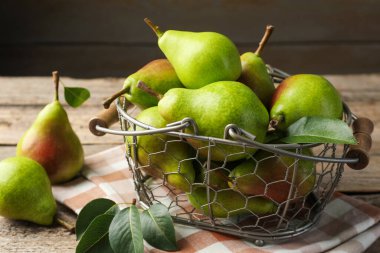 Metal sepetin içinde taze armutlar ve ahşap masanın üzerinde yeşil yapraklar, yakın plan.