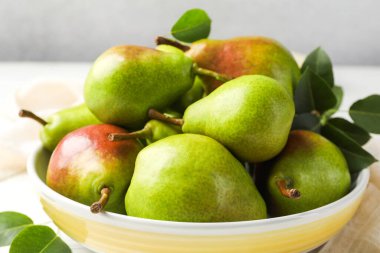 Taze armutlar kasede ve yeşil yapraklar masada, yakın plan.