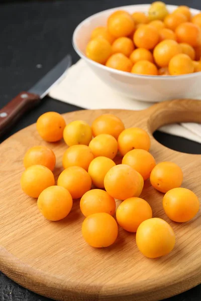 Olgun sarı kiraz erikleri, ahşap tahta ve bıçak siyah masada, yakın plan.