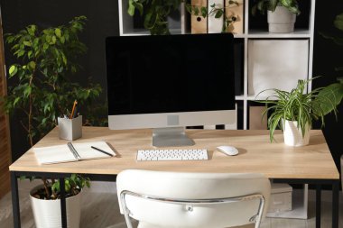 Modern bilgisayarı, kırtasiyesi ve çiçek dekoru olan şık bir iş yeri. Biyofilik iç tasarım