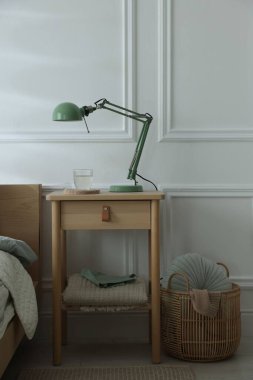 Yatak odasının yanında lamba ve bir bardak su olan komodinin yanında.