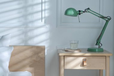 Yatak odasının yanında lamba ve bir bardak su olan komodinin yanında.