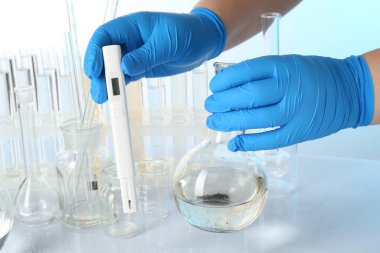 Su kalitesinin incelenmesi. Işık arka planına karşı masanda numune ve dijital pH ölçer bulunan bilim adamı, yakın plan