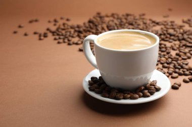 Kahverengi arka planda bir fincan sıcak kahve ve fasulye, yakın plan. Metin için boşluk