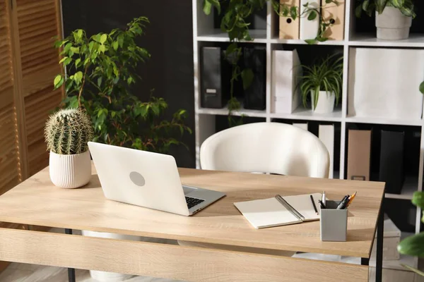 Ofisinde dizüstü bilgisayarı, kırtasiyesi ve çiçek dekoru olan şık bir iş yeri. Biyofilik iç tasarım