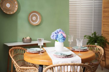 Yemek odasındaki ahşap masada, tabak ve vazo çiçekli şık bir ortam. İç tasarım