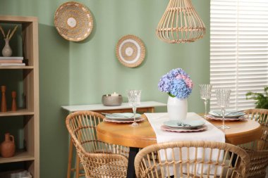 Yemek odasındaki ahşap masada, tabak ve vazo çiçekli şık bir ortam. İç tasarım