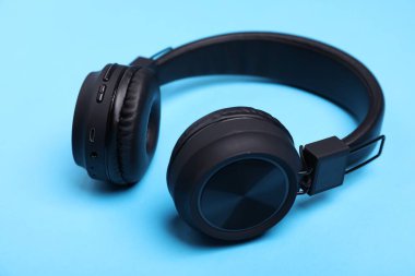 Açık mavi arka planda bir çift şık siyah kulaklık, yakın plan.