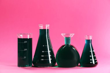 Pembe arka planda yeşil sıvı bulunan laboratuvar camları. Metin için boşluk