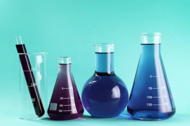 Turkuaz arka planda renkli sıvılar bulunan laboratuvar camları.