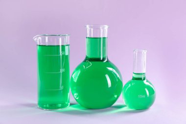 Eflatun arkaplanda yeşil sıvı bulunan laboratuvar camları.