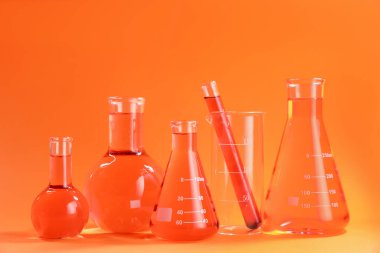 Turuncu zemin üzerinde renk sıvısı olan laboratuvar camları.