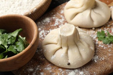 Ahşap tahtada pişmemiş khinkaliler (hamur tatlısı) ve maydanozlar, yakın plan.
