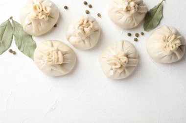 Beyaz masa üzerinde biber ve defne yapraklarıyla pişirilmemiş khinkaliler (hamur köfteleri). Metin için boşluk