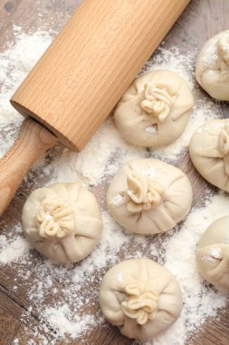 Ahşap masa üzerinde merdane ve un ile pişirilmemiş khinkaliler (hamur tatlısı) düz yatıyordu