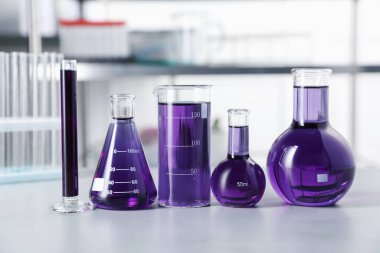 İçerideki ışık masasının üzerinde mor sıvı bulunan farklı bir laboratuvar camı.