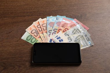 Akıllı telefon ve avro banknotları ahşap masanın üzerinde.