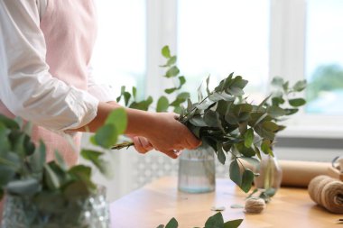 Çiçekçinin ahşap masasında okaliptüs dallarından güzel bir buket yapıyor.