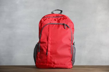 Ahşap masada gri arka planda kırmızı sırt çantası