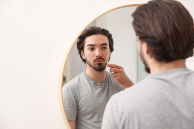 Akne sorunu olan genç bir adam evdeki aynanın yanındaki yüzüne krem sürüyor. Mesaj atmak için yer var.