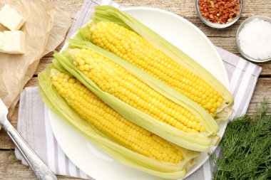 Lezzetli haşlanmış mısır koçanları, ahşap masada dereotu ve baharatlar.