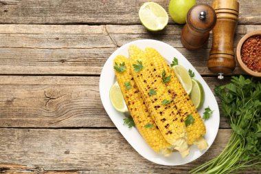 Lezzetli ızgara mısır koçanları maydanozlu ve ahşap masa üzerinde limon dilimleri, düz yatak. Metin için boşluk