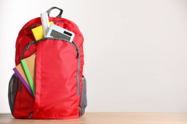 Ahşap masanın üzerinde farklı kırtasiye malzemelerinin bulunduğu kırmızı sırt çantası. Metin için boşluk