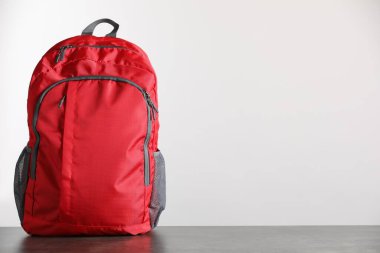 Gri masadaki kırmızı sırt çantası ışık arkaplanı, metin için boşluk