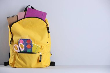 Sarı sırt çantası, ışık duvarının yanındaki masada farklı kırtasiye malzemesi var. Metin için boşluk