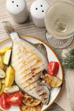 Hafif ahşap masada patates, domates ve limon dilimleriyle servis edilen kızarmış balık. Ev yapımı deniz ürünleri yemeği.