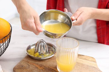 İçerideki beyaz mermer masada taze sıkılmış portakal suyunu bardağa dolduran kadın, yakın plan.