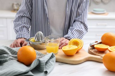 Meyve sıkacağı, taze sıkılmış portakal suyu ve meyveli bir kadın beyaz mermer masada, kapalı bir yerde.