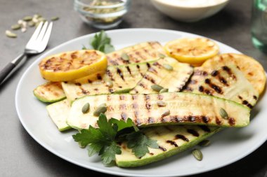 Lezzetli ızgara kabak dilimleri, balkabağı tohumları, limon ve maydanoz gri masada, yakın plan.