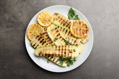 Lezzetli ızgara kabak dilimleri, balkabağı tohumları, limon ve maydanoz gri desenli masa, üst görünüm