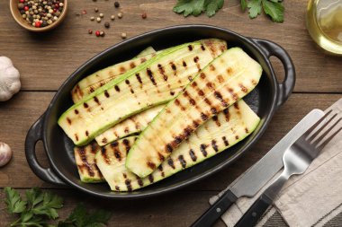 Lezzetli ızgara kabak dilimleri fırın tabağında, çatal bıçakta ve baharatlarda ahşap masada, düz yerde.