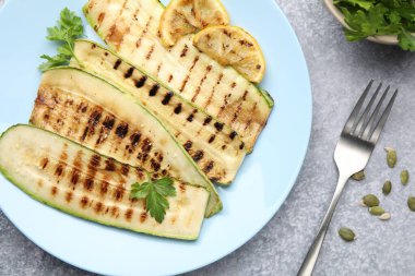 Lezzetli ızgara kabak dilimleri, maydanozlu ve limonlu gri desenli masada servis ediliyor.